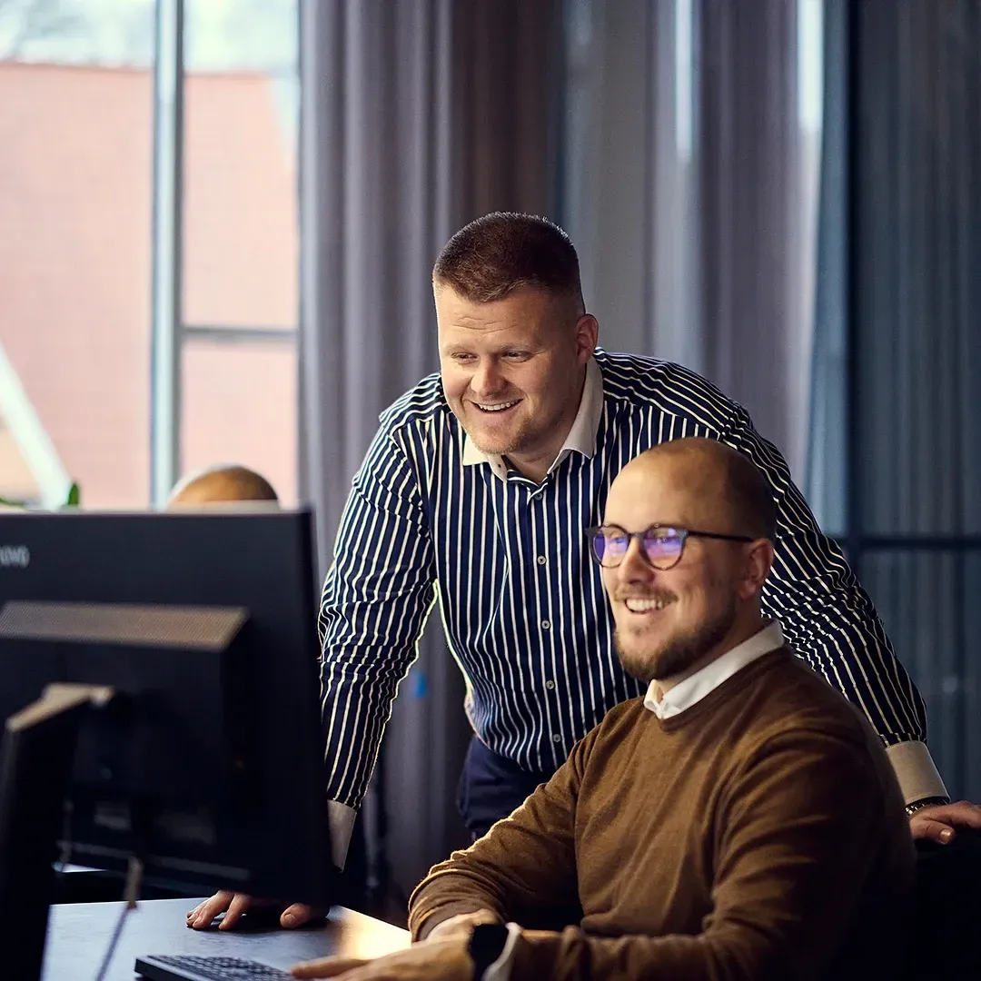 To mænd smiler, mens de kigger på en computerskærm på Homerunner-kontoret.