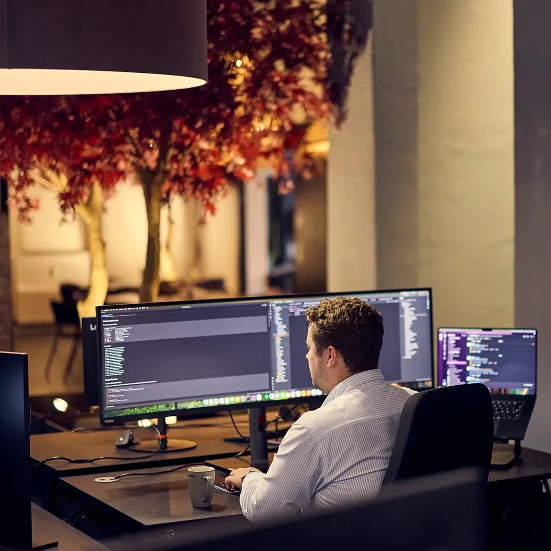 Man in a white shirt working on coding at a desk with two monitors.